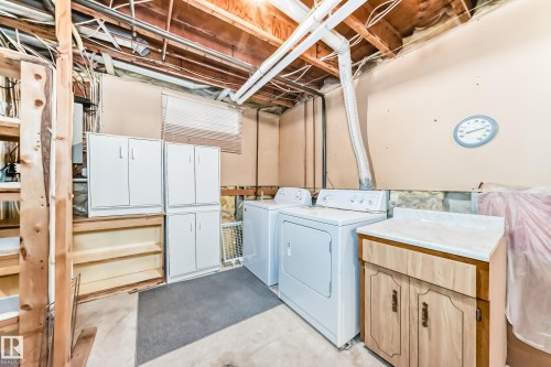 Laundry area featuring a washer and dryer, adjacent utility sink with a wood-finish vanity and integrated countertop, and exposed ceiling joists - 9528 189 Street, Edmonton, AB - Indoor Photo Showing Laundry Room