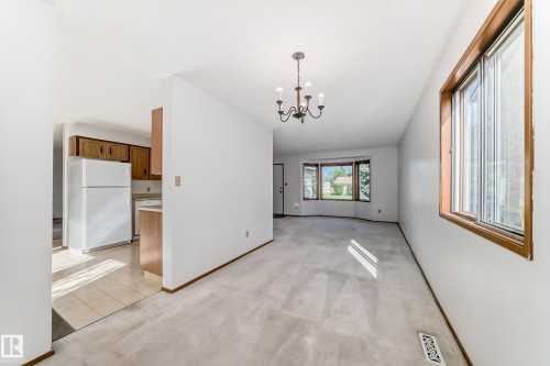 Spacious living area featuring light-colored carpeting, a multi-pane window with wood-finish trim, and a classic-style chandelier - 9528 189 Street, Edmonton, AB - Indoor Photo Showing Other Room