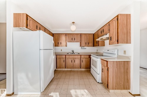 Kitchen featuring ample wood-finish cabinetry, light-toned countertops, and a full suite of white appliances including a refrigerator, range, and range hood - 9528 189 Street, Edmonton, AB - Indoor Photo Showing Kitchen With Double Sink