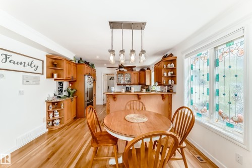 Bright dining area featuring hardwood flooring, a circular wooden dining table, and a contemporary linear pendant light fixture - 11115 44 Street, Edmonton, AB - Indoor Photo Showing Dining Room