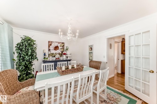 Dining area featuring wood-finish flooring, a white chandelier, crown molding, and French doors - 11115 44 Street, Edmonton, AB - Indoor Photo Showing Dining Room