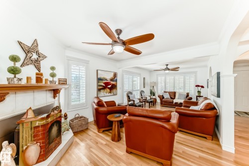 Living area featuring wood-finish flooring, a fireplace with a wood mantel, multiple ceiling fans, and window shutters - 11115 44 Street, Edmonton, AB - Indoor Photo Showing Living Room With Fireplace
