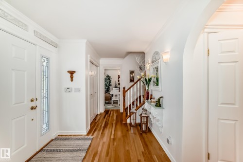 Foyer featuring a white paneled front door with a decorative glass sidelight, wood-finish flooring, a wood baluster staircase, a built-in archway, and wall sconces - 11115 44 Street, Edmonton, AB - Indoor Photo Showing Other Room