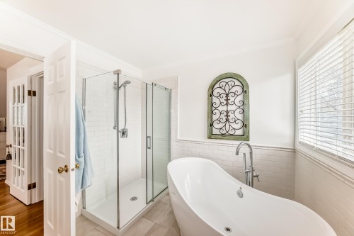 Freestanding soaking tub with floor-mounted faucet, glass-enclosed shower, white subway tile wainscoting, and large window with blinds - 11115 44 Street, Edmonton, AB - Indoor Photo Showing Bathroom