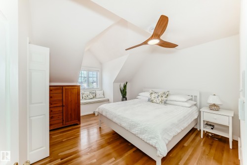 Attic room featuring a window seat with built-in storage, wood-finish flooring, a contemporary ceiling fan with integrated lighting, and white paneled walls - 11115 44 Street, Edmonton, AB - Indoor Photo Showing Bedroom