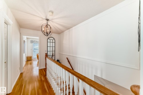 Hardwood flooring throughout the hallway, white painted walls, and a contemporary spherical chandelier - 11115 44 Street, Edmonton, AB - Indoor Photo Showing Other Room