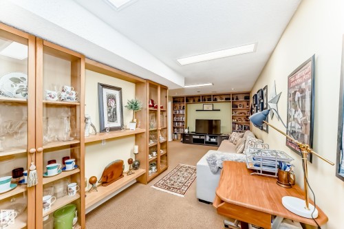 Recessed lighting illuminates a versatile interior featuring extensive built-in shelving, a full wall of wood-finish display cabinets with glass doors, and a built-in media center - 11115 44 Street, Edmonton, AB - Indoor