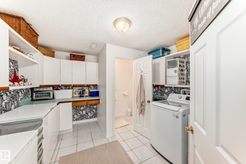 Well-appointed utility area featuring white cabinetry, solid surface countertops, and tile flooring - 11115 44 Street, Edmonton, AB - Indoor Photo Showing Laundry Room