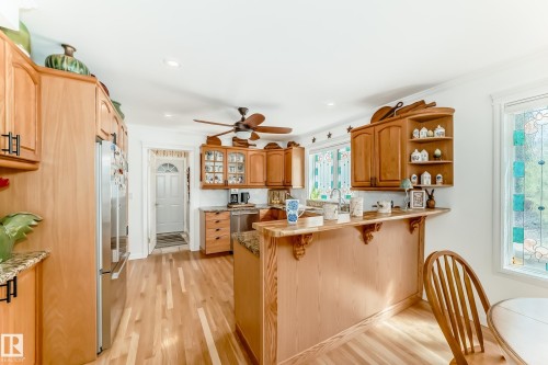 Kitchen featuring wood-finish flooring, light wood cabinetry with dark hardware, granite countertops, and stainless steel appliances - 11115 44 Street, Edmonton, AB - Indoor Photo Showing Other Room