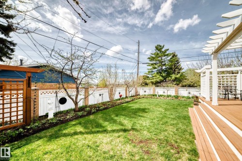 Expansive backyard featuring a manicured lawn, a two-tier wood deck with white pergola, and a decorative white lattice fence with brick columns - 11115 44 Street, Edmonton, AB - Outdoor