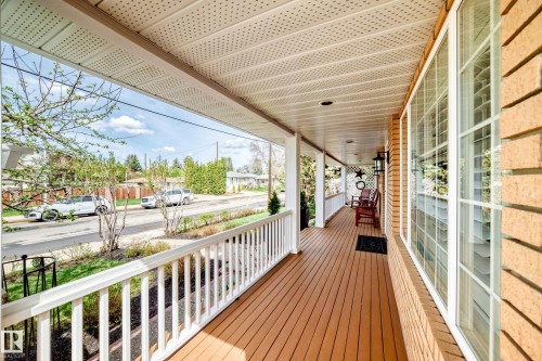 Expansive covered front porch featuring wood-finish flooring, white railing, recessed lighting, and a brick exterior facade - 11115 44 Street, Edmonton, AB - Outdoor With Deck Patio Veranda With Exterior