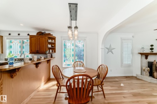 Dining area featuring a wood-finish table, plank flooring, and a multi-bulb linear pendant light fixture - 11115 44 Street, Edmonton, AB - Indoor Photo Showing Dining Room With Fireplace