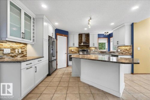 Kitchen featuring white cabinetry, stone tile backsplash, stainless steel appliances, granite countertops, and tile flooring - 11824 13 Avenue, Edmonton, AB - Indoor Photo Showing Kitchen With Upgraded Kitchen