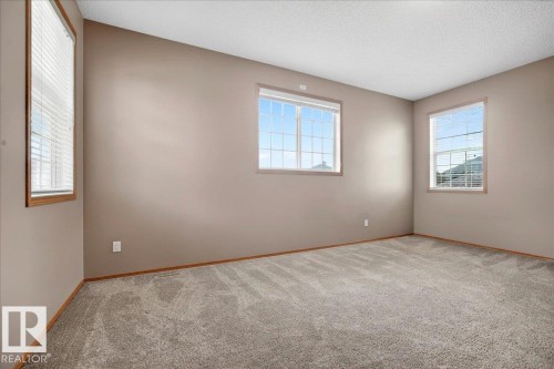 Spacious room featuring neutral-toned walls, plush grey carpeting, and two large windows with horizontal blinds and wood trim - 11824 13 Avenue, Edmonton, AB - Indoor Photo Showing Other Room