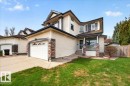 Cream-colored siding exterior featuring a covered front porch with stone accents, an attached garage with decorative windows, a concrete driveway, and a front lawn with established landscaping - 11824 13 Avenue, Edmonton, AB  - Outdoor 