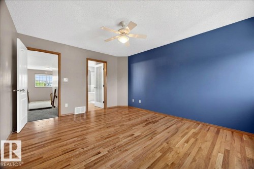 Spacious room featuring hardwood flooring, a blue accent wall, neutral-toned walls, and a ceiling fan with integrated lighting - 11824 13 Avenue, Edmonton, AB - Indoor Photo Showing Other Room