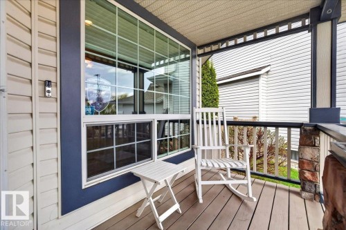 Covered porch featuring light-colored siding, a large multi-pane window with dark trim, composite decking, and a stone-clad support pillar - 11824 13 Avenue, Edmonton, AB - Outdoor With Deck Patio Veranda With Exterior