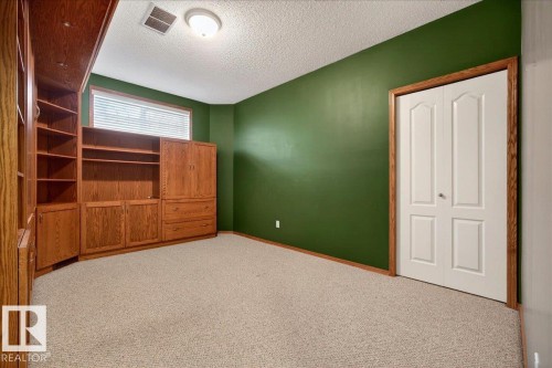 Built-in custom cabinetry and shelving unit with a wood finish, complemented by neutral carpeting and a window with horizontal blinds - 11824 13 Avenue, Edmonton, AB - Indoor
