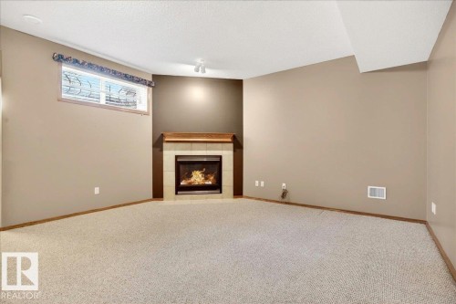 Carpeted room featuring a corner fireplace with a tile surround and wood mantel - 11824 13 Avenue, Edmonton, AB - Indoor Photo Showing Other Room With Fireplace