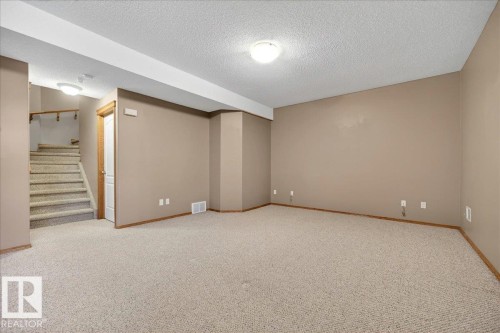 Spacious carpeted room featuring a neutral color palette, recessed lighting, and a visible staircase with wood-finish railing - 11824 13 Avenue, Edmonton, AB - Indoor