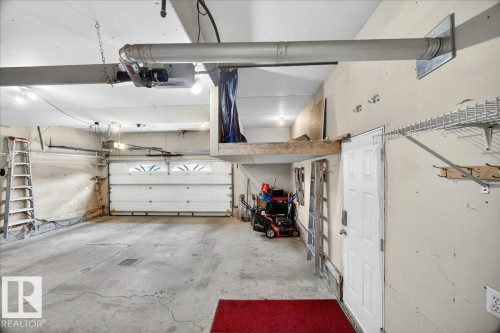Spacious garage with a sectional overhead door featuring decorative window inserts, an additional side entry door, and overhead lighting - 11824 13 Avenue, Edmonton, AB - Indoor Photo Showing Garage