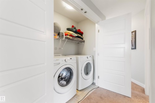 The property includes a laundry area with a white front-loading washing machine and dryer, a wire shelf, and tile flooring - 607 40 Street Sw, Edmonton, AB - Indoor Photo Showing Laundry Room