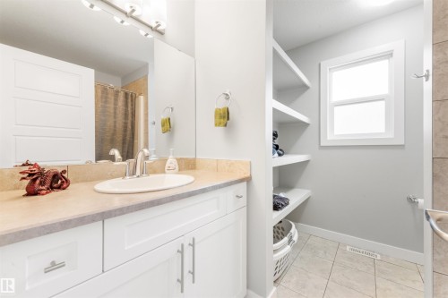 Well-appointed bathroom featuring a vanity with a light-colored countertop and white cabinetry, a large mirror, and open shelving for storage - 607 40 Street Sw, Edmonton, AB - Indoor