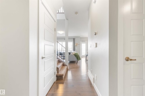 This interior entryway features hardwood flooring and white walls, leading to a carpeted staircase with dark railings - 607 40 Street Sw, Edmonton, AB - Indoor Photo Showing Other Room
