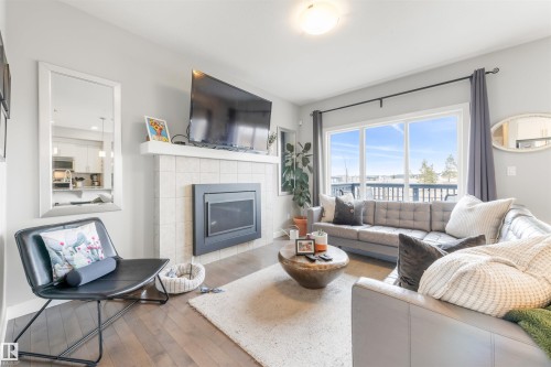 Living area featuring hardwood floors, a tiled fireplace, and a large window providing ample natural light and views of the outdoors - 607 40 Street Sw, Edmonton, AB - Indoor Photo Showing Living Room With Fireplace
