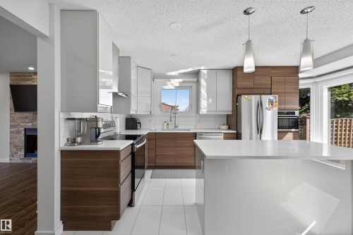 Modern kitchen featuring a central island, white subway tile backsplash, stainless steel appliances, and two-tone cabinetry with wood-finish and high-gloss white elements - 15251 88A Street, Edmonton, AB - Indoor Photo Showing Kitchen With Upgraded Kitchen