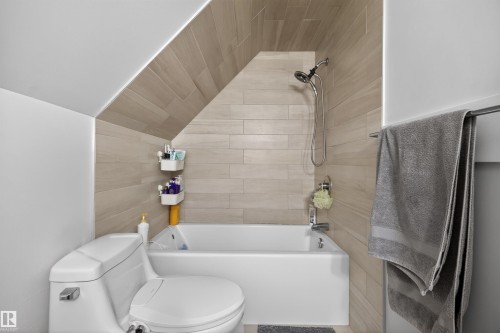 Bathroom featuring a white bathtub, toilet, and tiled walls extending to a sloped ceiling - 15251 88A Street, Edmonton, AB - Indoor Photo Showing Bathroom