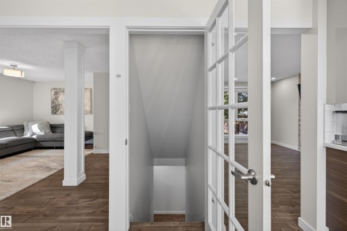 Stairwell entry featuring white French doors with polished chrome hardware, wood-finish flooring, and white baseboards - 15251 88A Street, Edmonton, AB - Indoor Photo Showing Other Room
