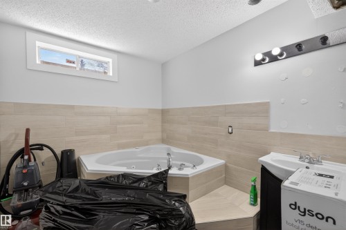 Corner jetted bathtub with a tiled surround, complemented by light-toned wall tiling - 15251 88A Street, Edmonton, AB - Indoor Photo Showing Bathroom