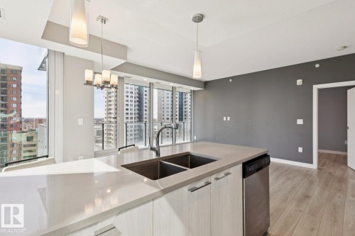 Modern kitchen island featuring a double-basin sink and integrated stainless steel dishwasher - #1601 10180 103 St Nw, Edmonton, AB - Indoor Photo Showing Kitchen With Double Sink