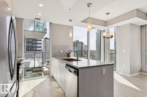 Modern kitchen featuring expansive floor-to-ceiling windows, a central island with an undermount sink, pendant lighting, built-in dishwasher, and light wood-finish flooring - #1601 10180 103 St Nw, Edmonton, AB - Indoor Photo Showing Kitchen With Double Sink With Upgraded Kitchen