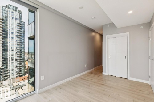 Contemporary interior featuring a wide window, light wood-finish flooring, recessed lighting, a sliding barn door, and a modern city backdrop - #1601 10180 103 St Nw, Edmonton, AB - Indoor Photo Showing Other Room