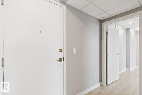 Entryway featuring a white door with brass hardware, light gray painted walls, a dropped ceiling, and light wood-finish flooring - #1601 10180 103 St Nw, Edmonton, AB - Indoor Photo Showing Other Room