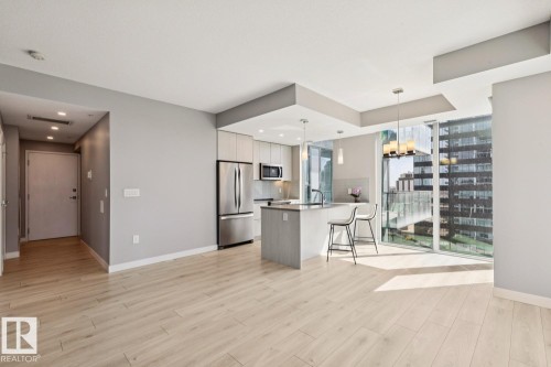 Open-concept kitchen and living area featuring wood-finish flooring, a kitchen island with seating, stainless steel appliances, and floor-to-ceiling windows - #1601 10180 103 St Nw, Edmonton, AB - Indoor Photo Showing Other Room