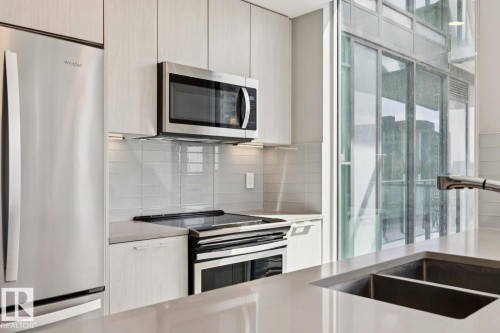 Modern kitchen featuring stainless steel appliances, light wood-finish cabinetry, a subway tile backsplash, and a large sink with a gooseneck faucet - #1601 10180 103 St Nw, Edmonton, AB - Indoor Photo Showing Kitchen With Double Sink With Upgraded Kitchen