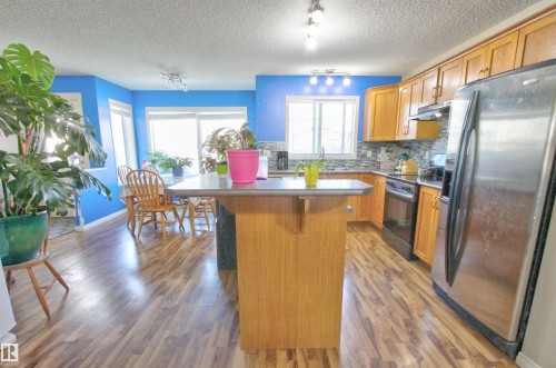 Kitchen featuring wood-finish flooring, a central island with countertop seating, stainless steel refrigerator, and wood cabinetry - 14820 140 Street, Edmonton, AB - Indoor Photo Showing Kitchen With Stainless Steel Kitchen