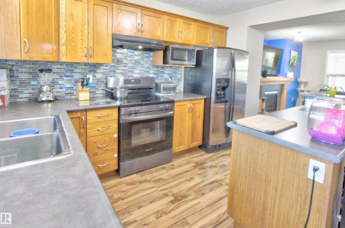Kitchen featuring wood cabinetry, stainless steel appliances, a mosaic tile backsplash, and wood-finish flooring - 14820 140 Street, Edmonton, AB - Indoor Photo Showing Kitchen