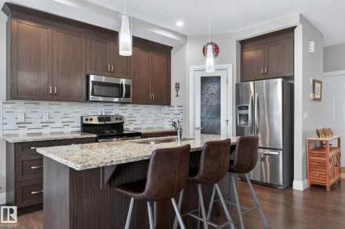 Modern kitchen featuring dark wood-finish cabinetry, granite countertops, and stainless steel appliances - 83 Sandalwood Place, Leduc, AB - Indoor Photo Showing Kitchen With Upgraded Kitchen