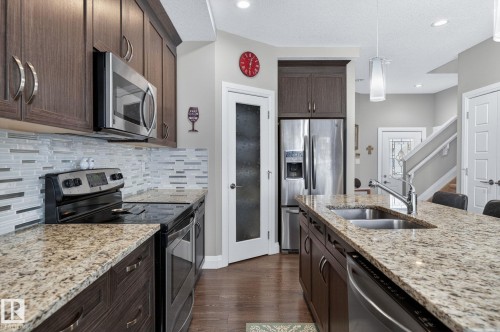 Kitchen featuring wood-finish cabinetry, granite countertops, stainless steel appliances, and a mosaic tile backsplash - 83 Sandalwood Place, Leduc, AB - Indoor Photo Showing Kitchen With Double Sink With Upgraded Kitchen