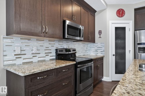 Kitchen featuring dark wood-finish cabinetry, light-toned stone countertops, and a mosaic tile backsplash - 83 Sandalwood Place, Leduc, AB - Indoor Photo Showing Kitchen With Double Sink With Upgraded Kitchen