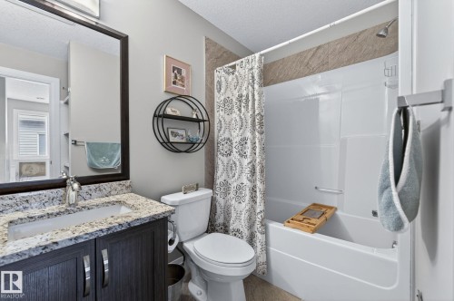 Bathroom featuring a white tub with shower, a vanity with a light granite countertop, and dark wood-finish cabinetry - 83 Sandalwood Place, Leduc, AB - Indoor Photo Showing Bathroom