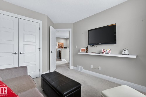 Carpeted room featuring a wall-mounted television and a floating shelf - 83 Sandalwood Place, Leduc, AB - Indoor