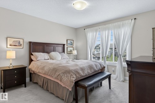 Carpeted room featuring a large window with white blinds and drapes, a central ceiling light fixture, and light-toned walls - 83 Sandalwood Place, Leduc, AB - Indoor Photo Showing Bedroom
