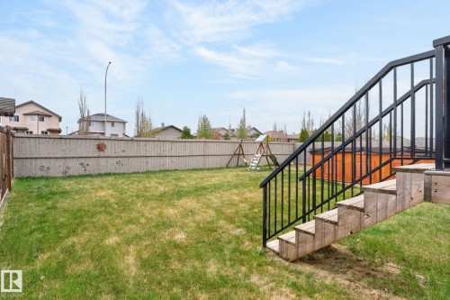 Expansive backyard featuring a manicured lawn, a full privacy fence, and wood steps with black metal railings - 83 Sandalwood Place, Leduc, AB - Outdoor