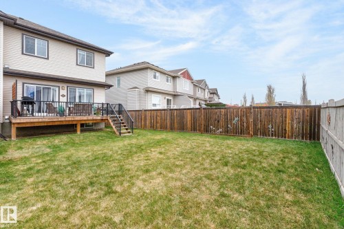 Spacious backyard featuring a wooden deck with dark railing, a wooden privacy fence, and a green lawn - 83 Sandalwood Place, Leduc, AB - Outdoor With Deck Patio Veranda