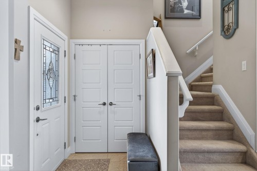 Entryway featuring a white door with decorative glass inserts, square panel bi-fold doors, and a carpeted staircase with a white wooden banister - 83 Sandalwood Place, Leduc, AB - Indoor Photo Showing Other Room